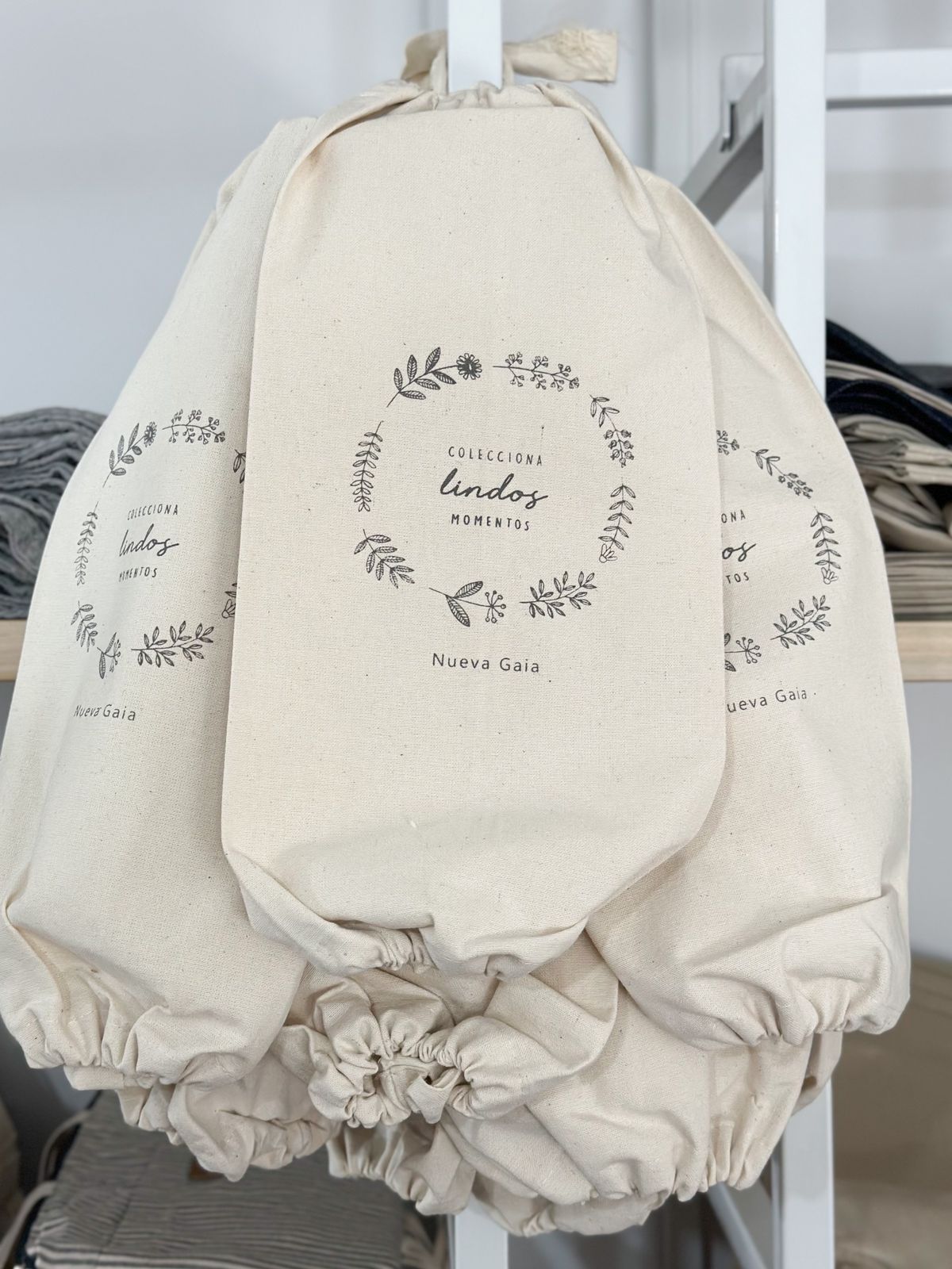 Bolsas de tela y toallas colgadas debajo de un estante con cajas y botellas grises y blancas.