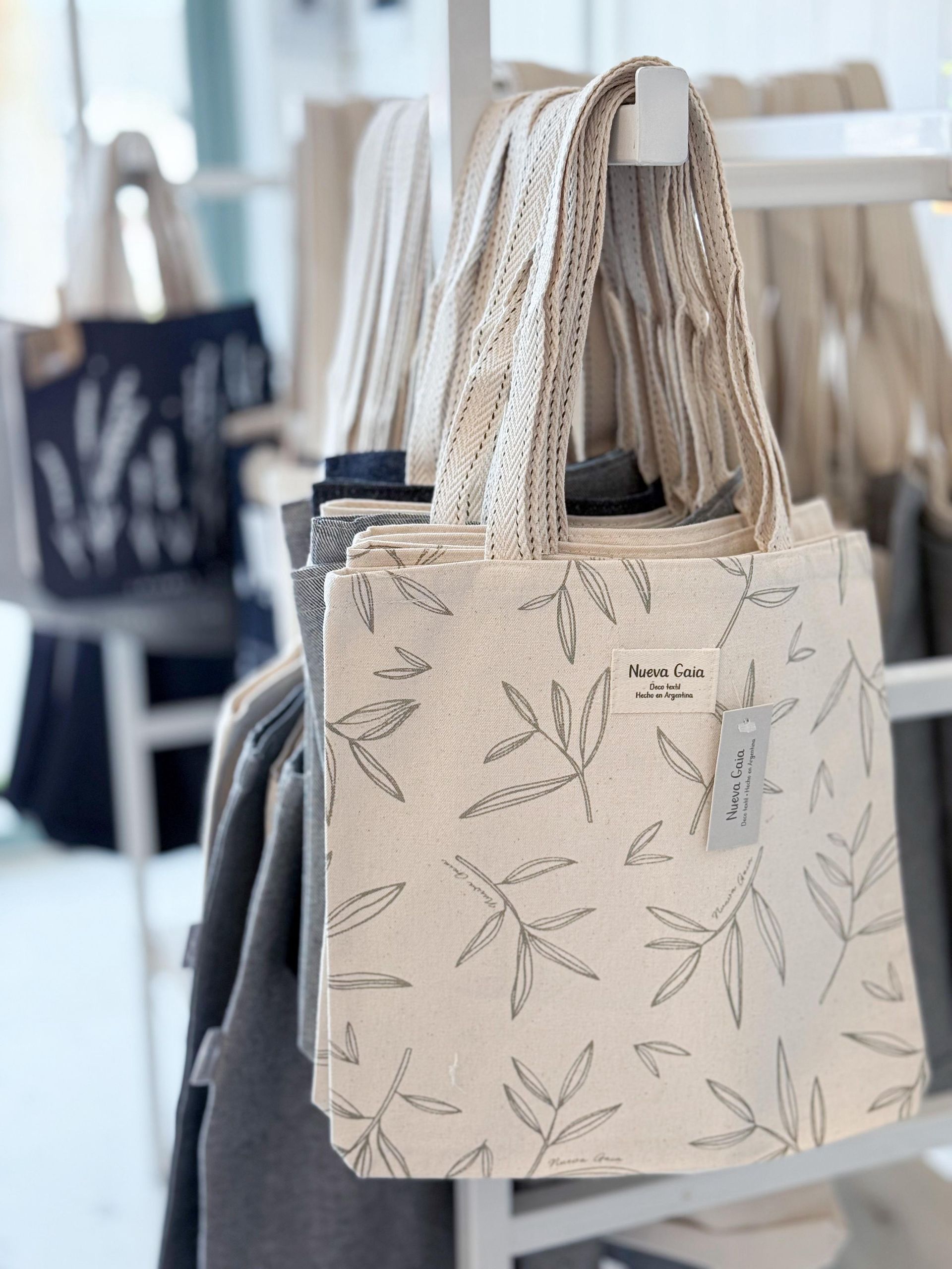 Bolso tote beige estampado con asas de cuerda colgado en un escaparate luminoso de una boutique.