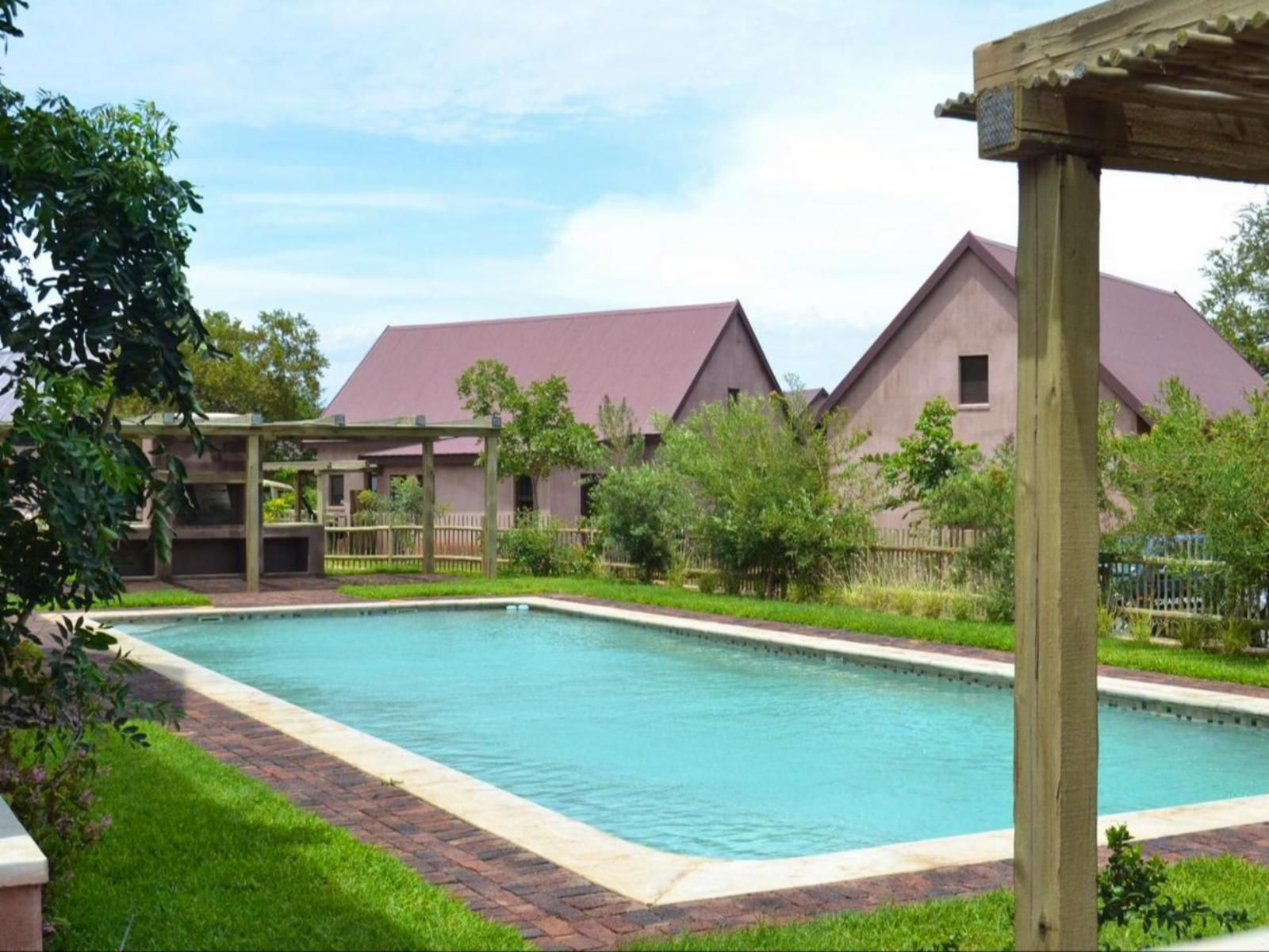 Swimming pool in front of two tan buildings with a red roof, under a partly cloudy sky.