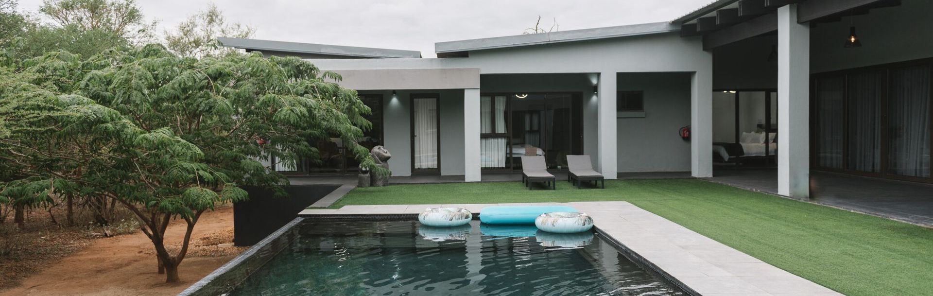 AM Villa Hoedspruit Wildlife Estate Modern house with a pool and a green lawn. A tree on the left, lounge chairs on the right.