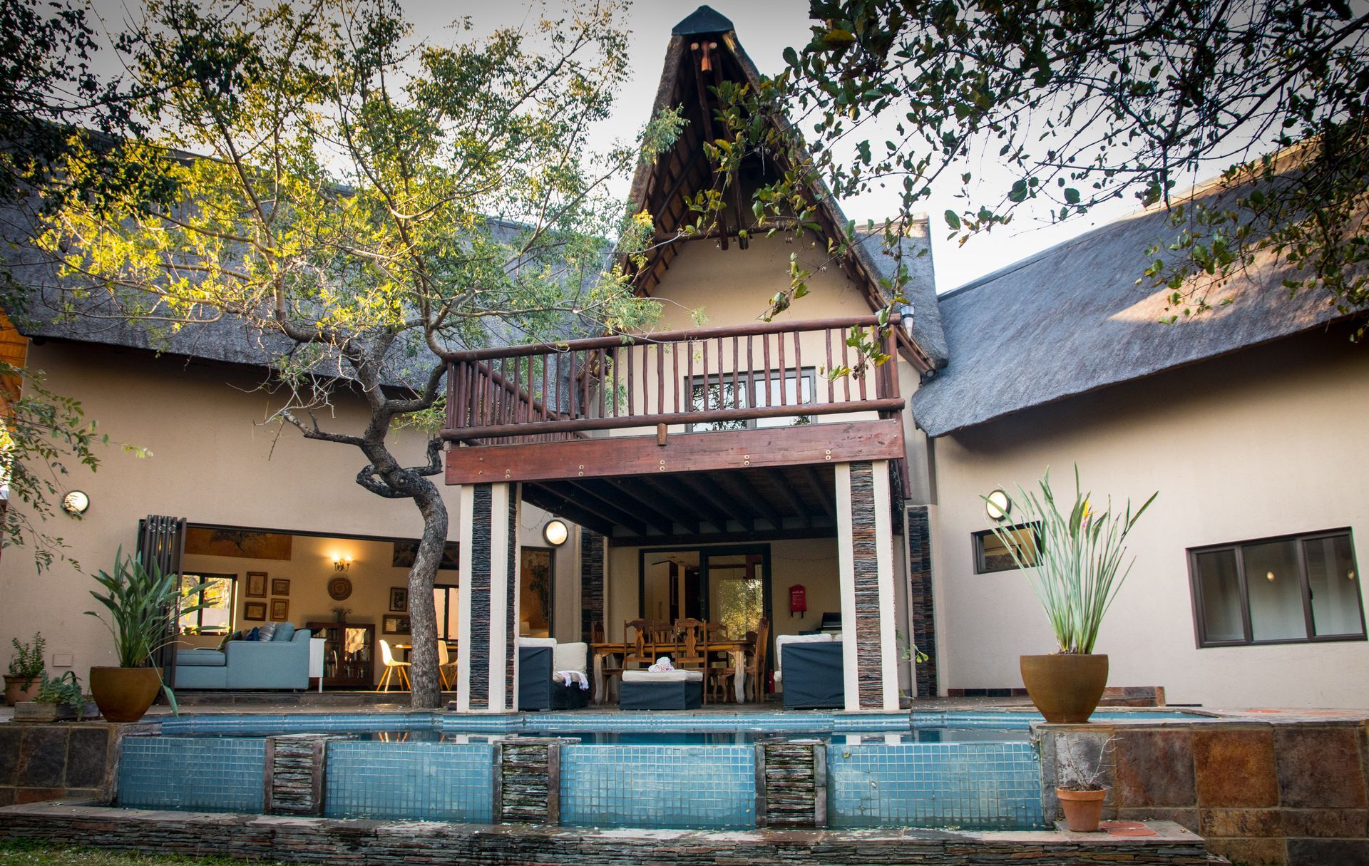 Hoedspruit Accommodation Luxury lodge exterior with pool, thatch roof, and balcony surrounded by trees.