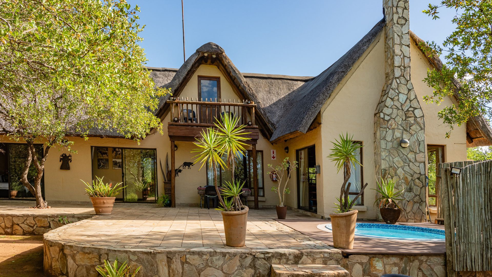 House with thatched roof, small pool, and stone patio. Exterior shot in sunny environment.