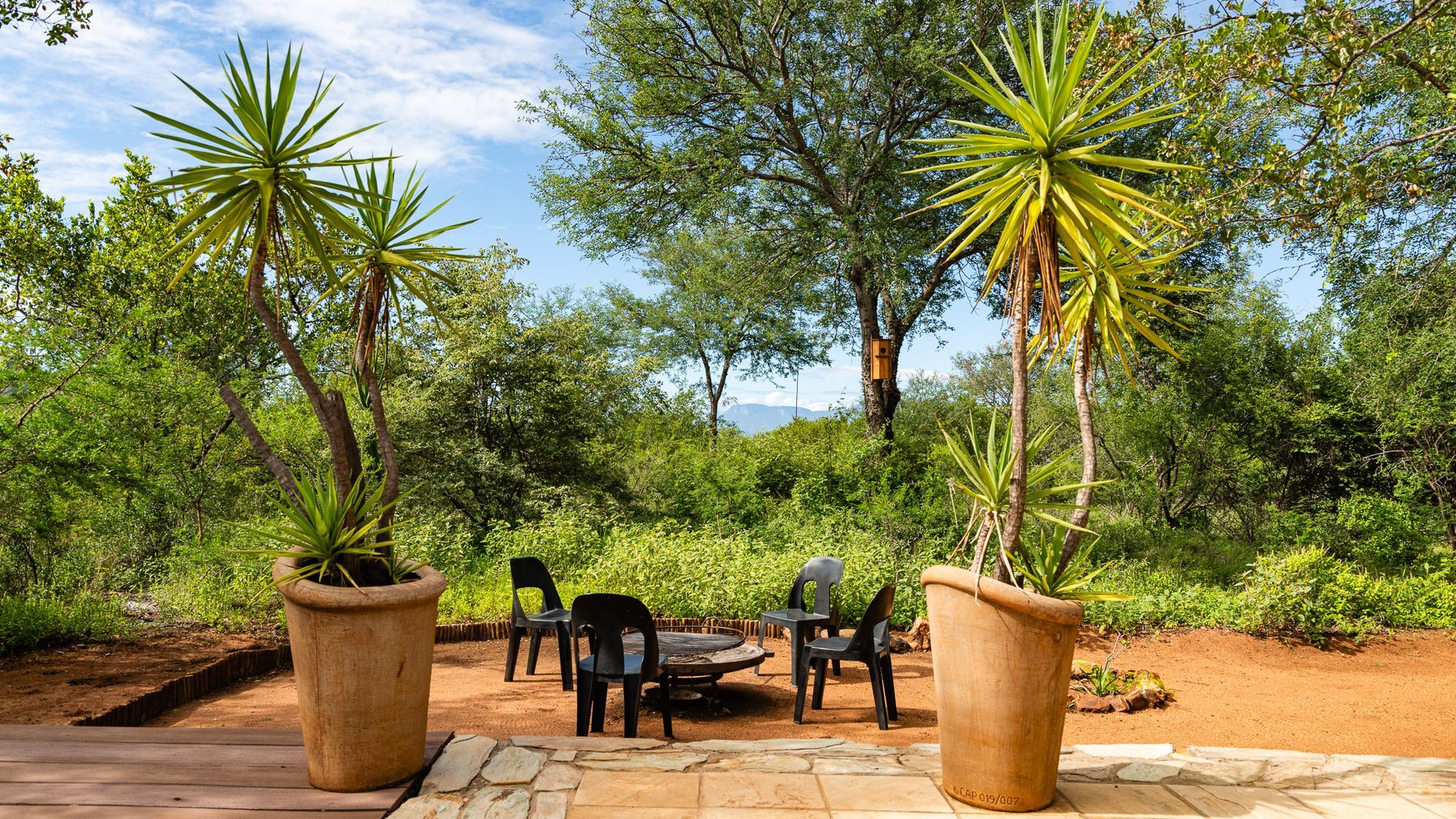 Outdoor seating area with potted palm trees, black chairs, and a fire pit, surrounded by lush greenery.