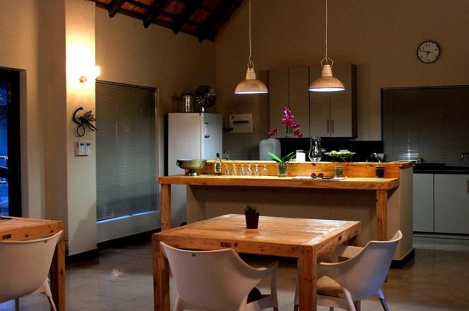 Dining area with wooden table and chairs, leading to a kitchen with overhead lights.