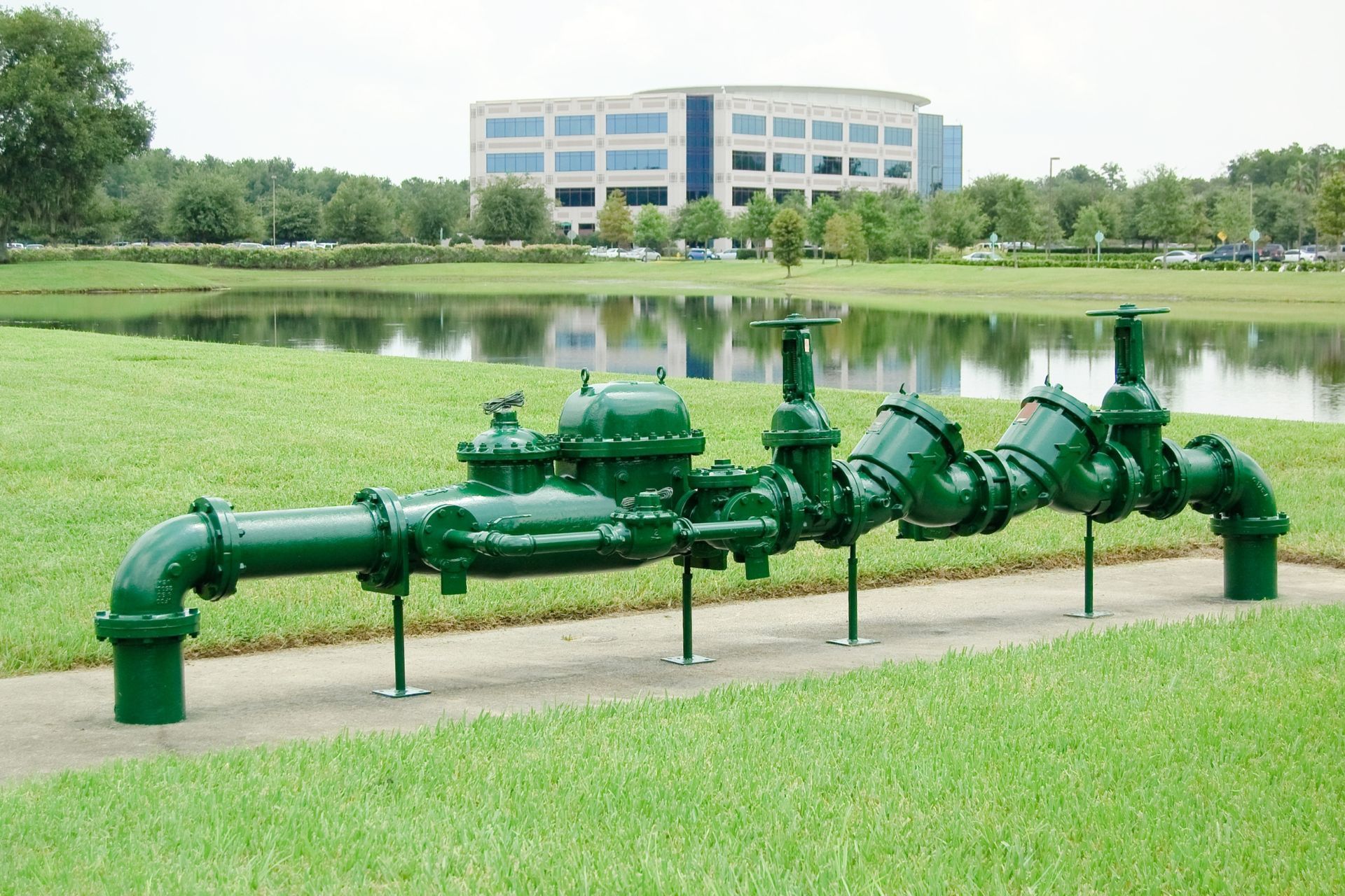 Green industrial pipes beside a pond with a building in the background
