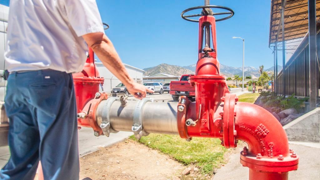 Worker inspecting large red industrial pipes and valves outdoors under a clear blue sky