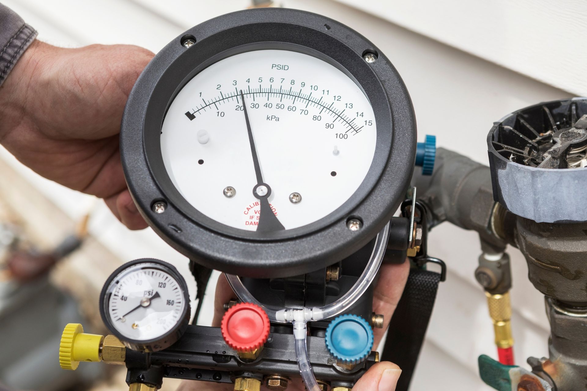 HVAC manifold gauge set with black dial and colored valves being held in a hand