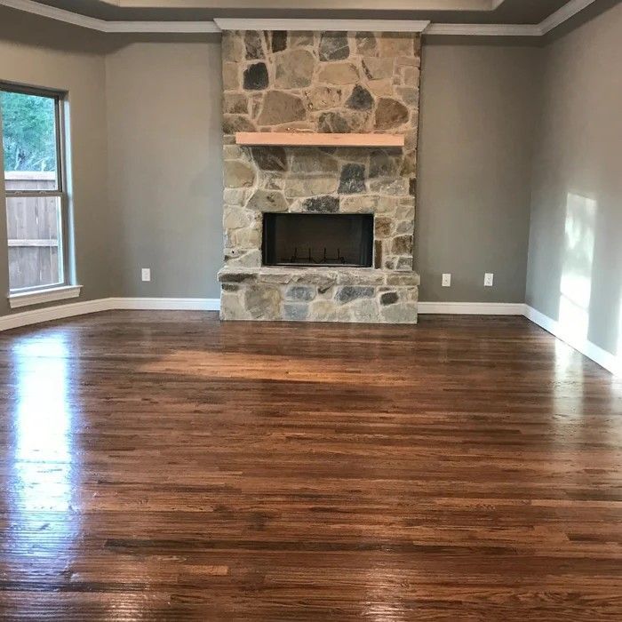 Empty living room with hardwood floors and a stone fireplace centered on the far wall