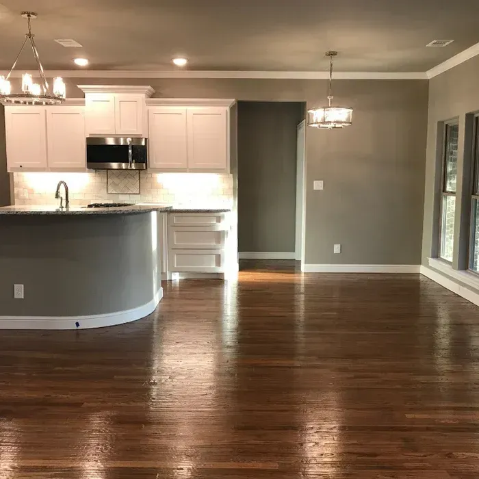 Empty open-plan kitchen and living area with hardwood floors, white cabinets, and gray walls.