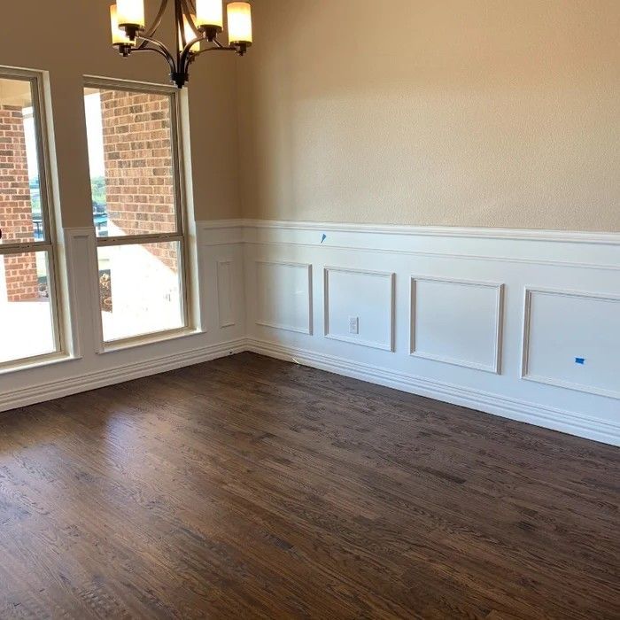 Empty dining room with dark wood floors, white wainscoting, and large windows