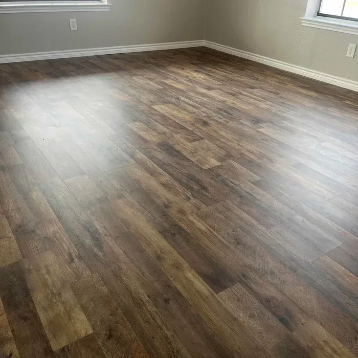 Empty room with wood-look flooring, gray walls, and sunlight from windows.