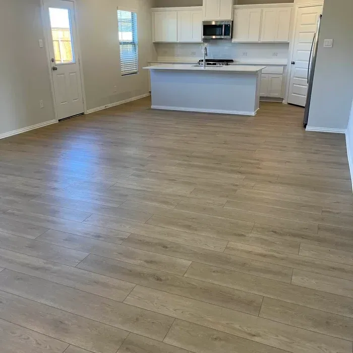 Empty modern kitchen and living area with light wood floors, white cabinets, and a central island.