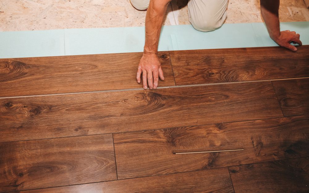 Person installing brown wood flooring with a hand tool, top-down view