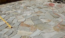 Stone patio under construction with irregular flagstones, a yellow tool handle, and an orange hose or cable.