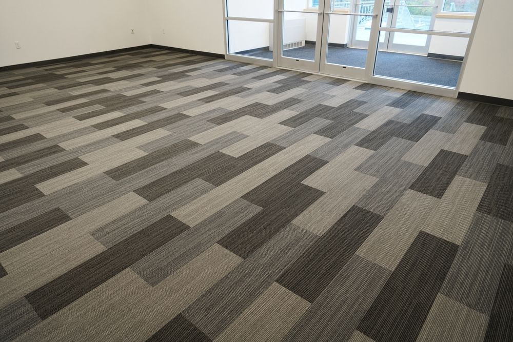 Empty office room with gray patterned carpet and glass doors in the background