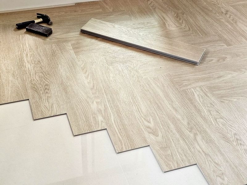 Light wood flooring planks being installed, with a measuring tool and cutter on the floor