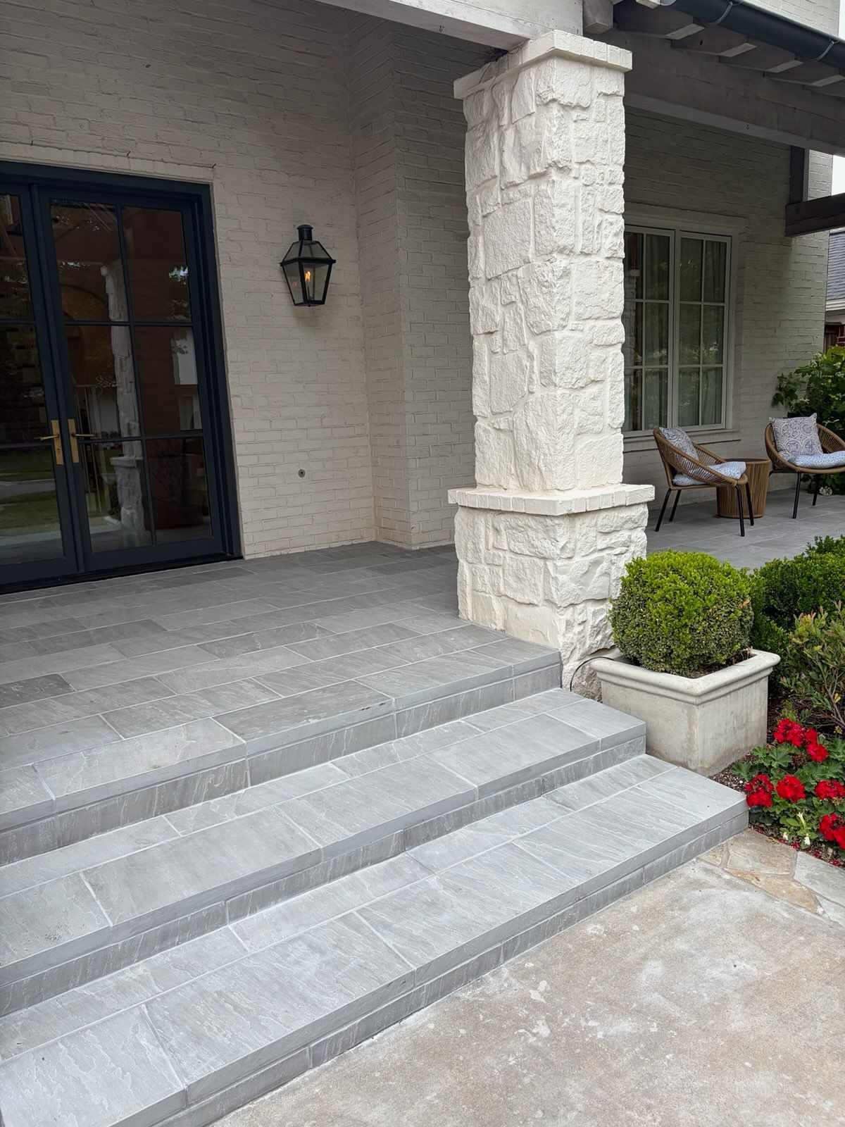 Front porch with gray stone steps, white columns, and potted flowers beside a house entrance