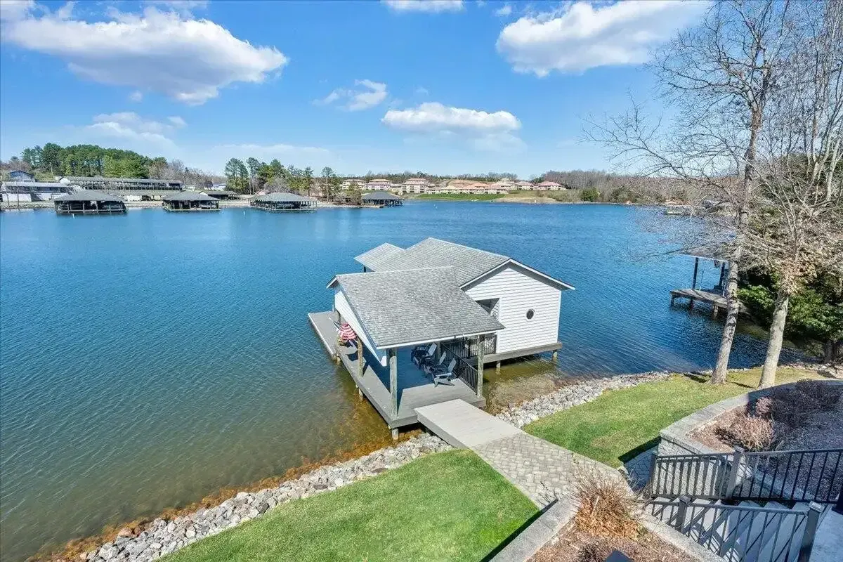 Covered dock on a calm blue lake with a walkway, green lawn, and houses in the distance