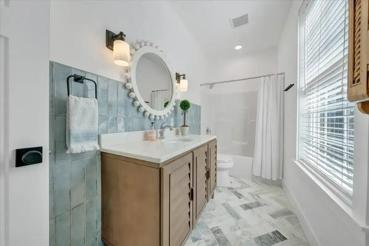 Bright bathroom with double vanity, oval mirror, glass shower, and white tile flooring