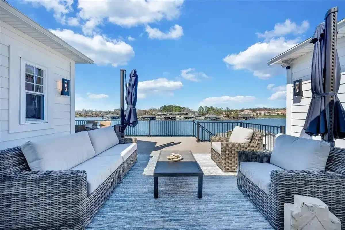 Waterfront patio with wicker seating, blue cushions, and ocean view between two white houses