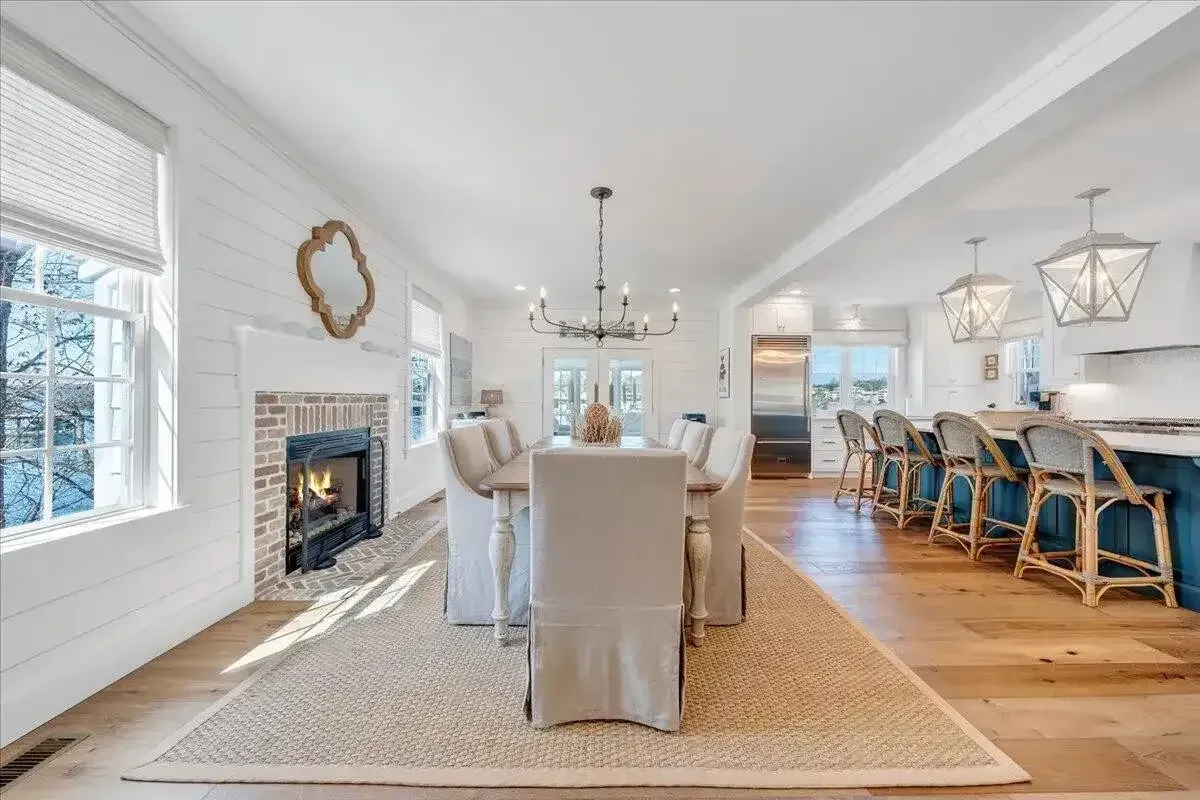 Bright dining room with white walls, fireplace, chandelier, and blue bar stools beside a wooden table