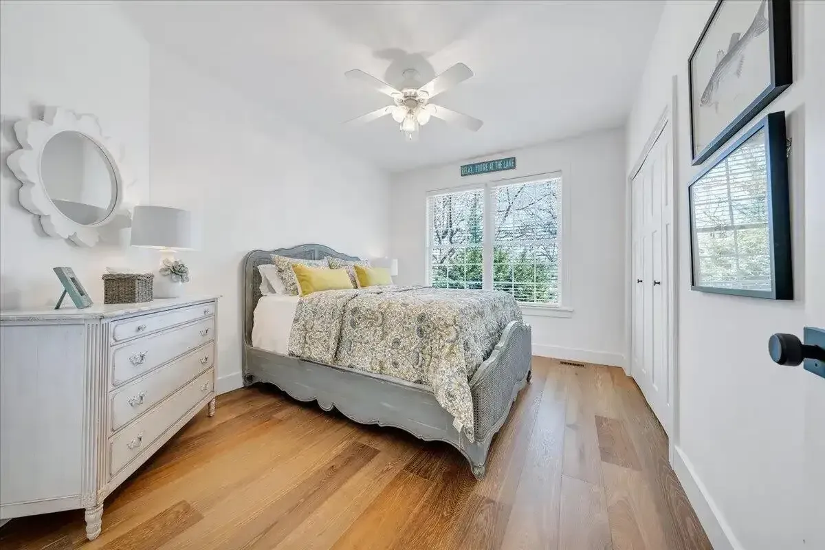 Bright bedroom with a bed, white dresser, hardwood floors, and large windows.