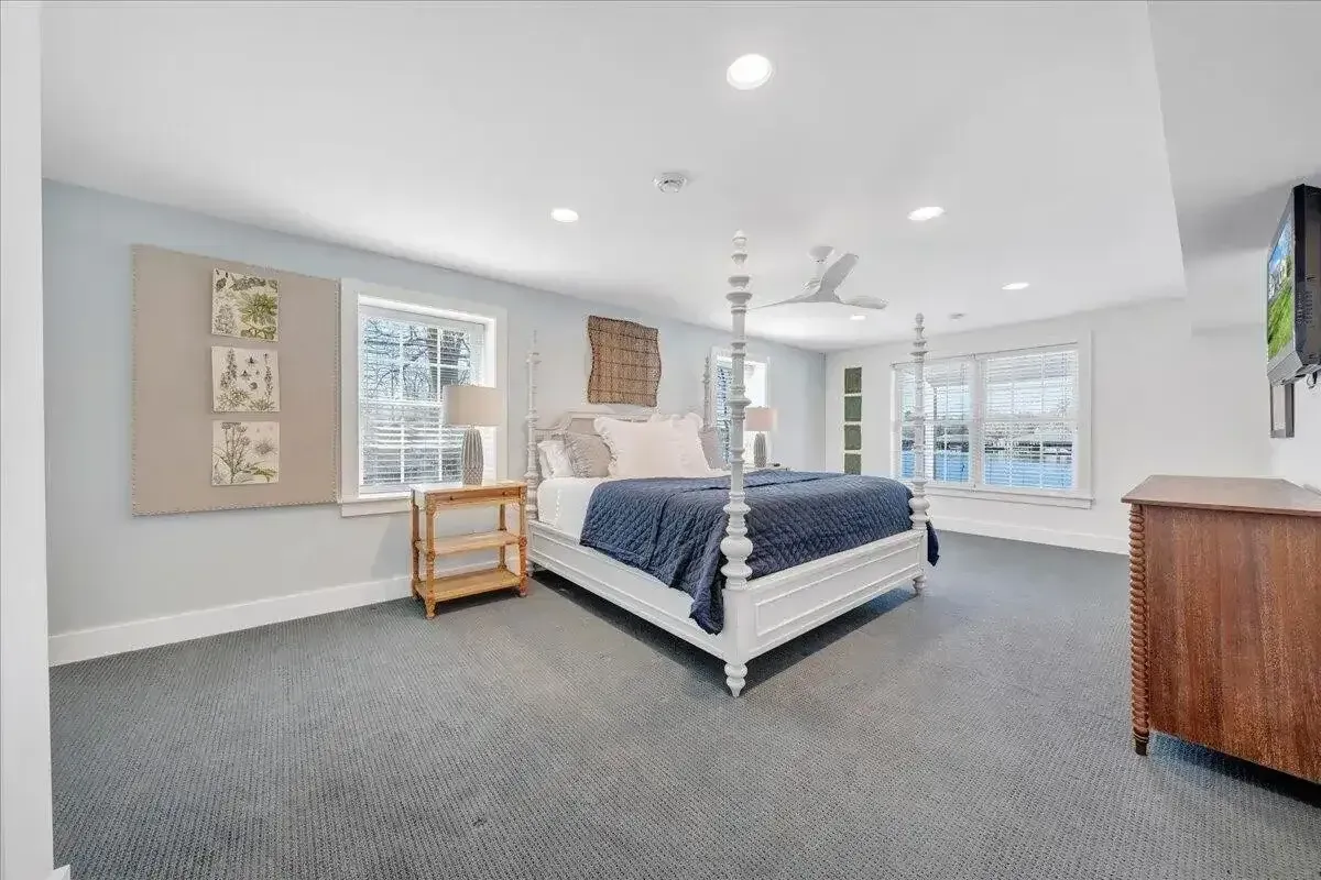 Spacious carpeted bedroom with a king bed, white walls, large windows, and a dresser