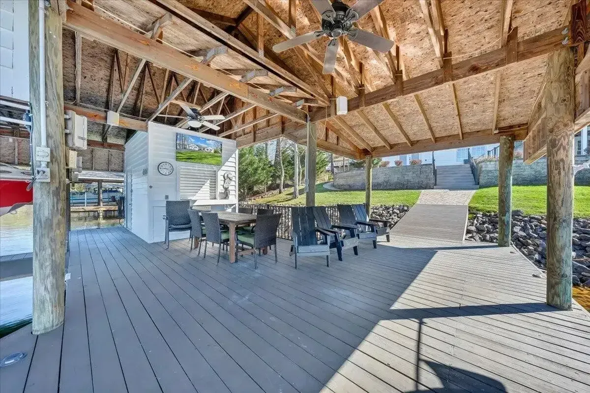 Covered outdoor deck with tables and chairs under a thatched roof, overlooking a grassy lawn