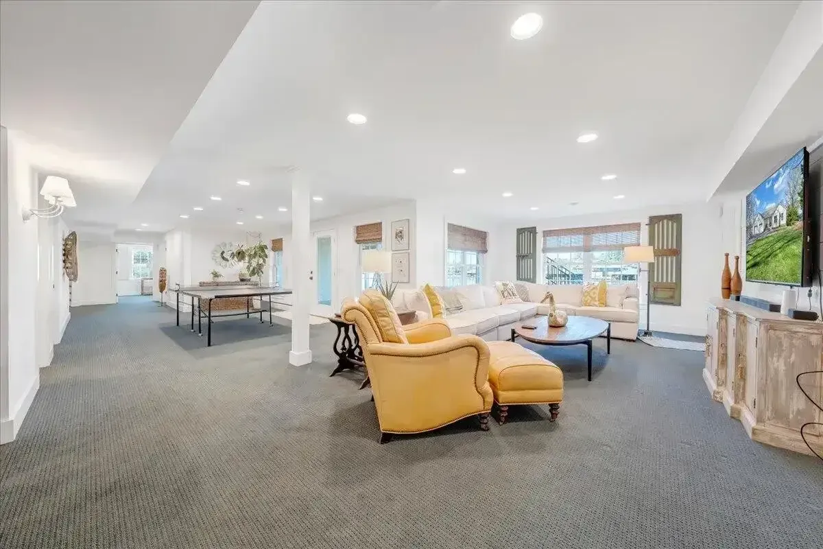 Bright open living room with yellow chairs, gray carpet, white walls, and a wall-mounted TV.