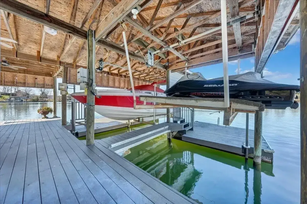 Covered wooden dock with kayaks on lifts over calm green water, beside a bright blue lake