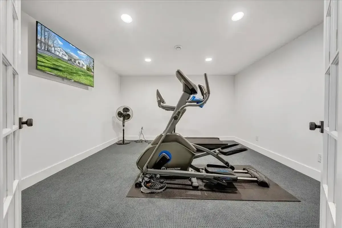 Small home gym with an exercise bike, treadmill, wall-mounted TV, and white walls