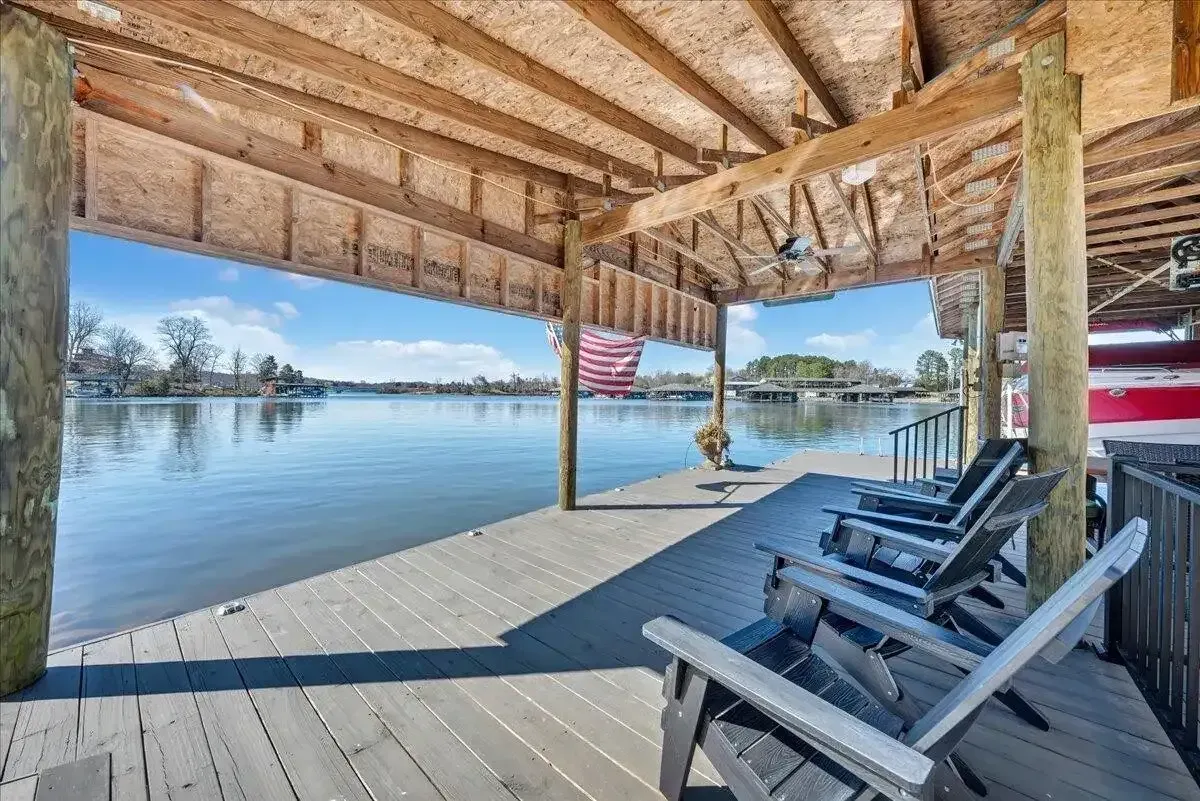 Covered wooden dock with lounge chairs overlooking a calm lake and distant shoreline