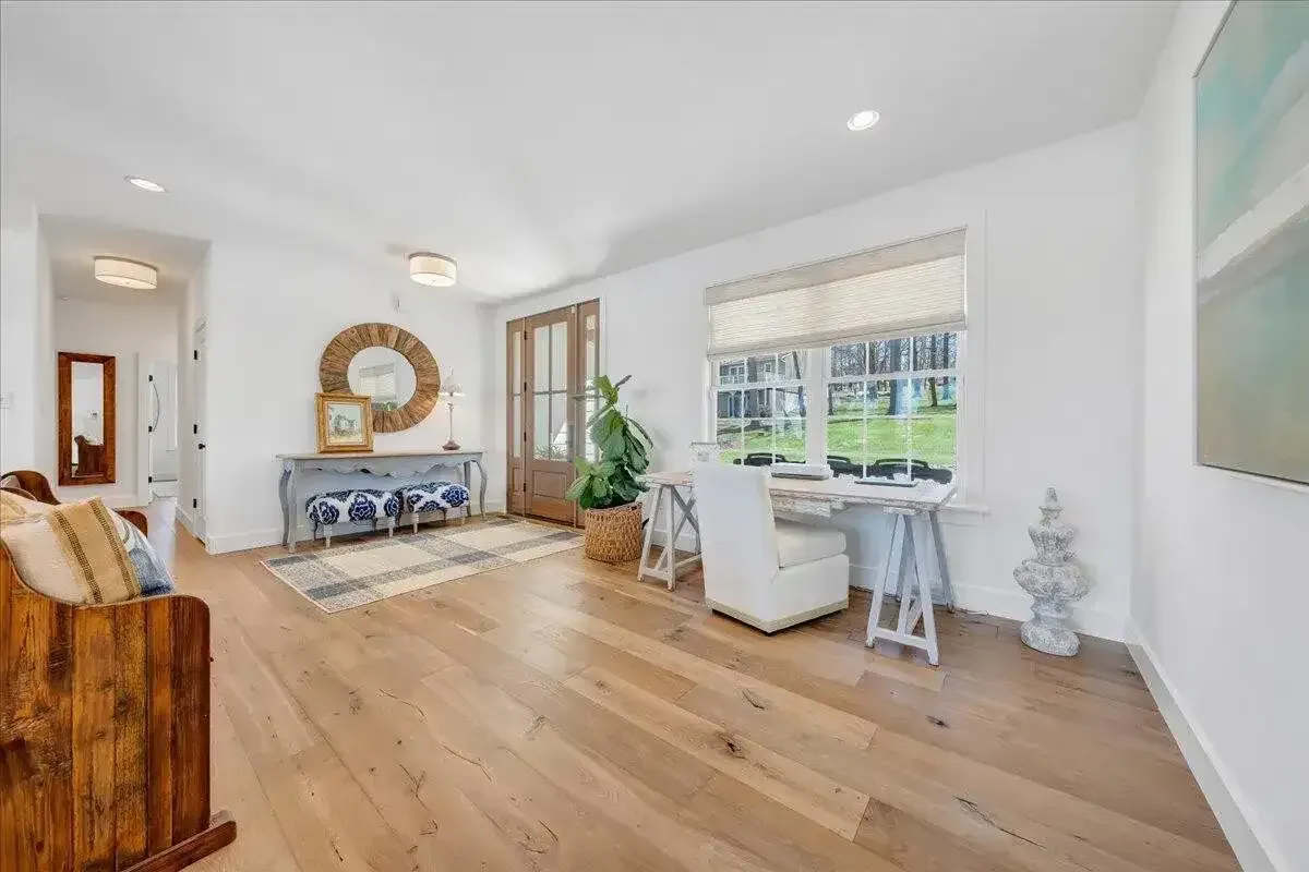 Bright living room with wood floors, white walls, sofa, bench, plants, and large windows