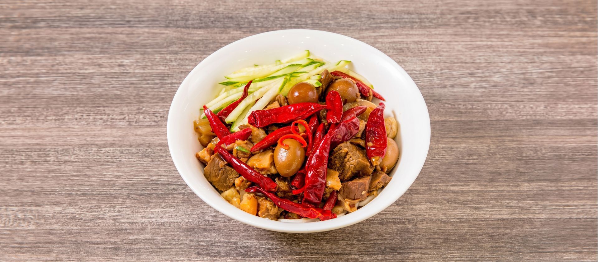 Bowl of spicy stir-fried noodles with red chilies and vegetables on a wooden table