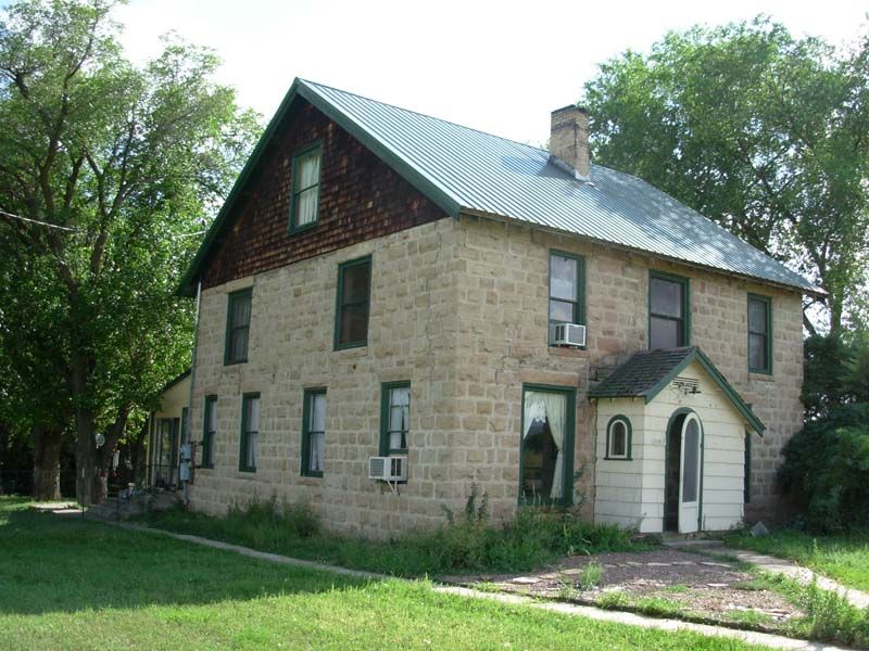 Stone house with green roof and white arched doorway, surrounded by trees and grass.