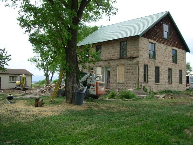 Two-story brick house under construction beside a large tree, with construction equipment and a grassy yard.