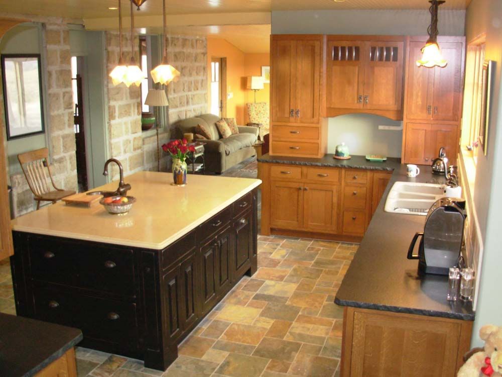 Warm kitchen with wooden cabinets, island counter, tiled floor, and stainless appliances under pendant lights