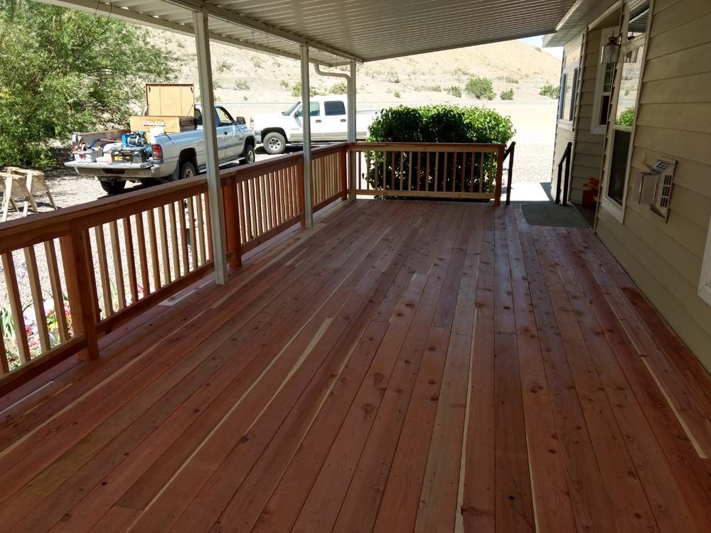 Covered wooden porch with reddish deck boards, railing, and outdoor street view beyond