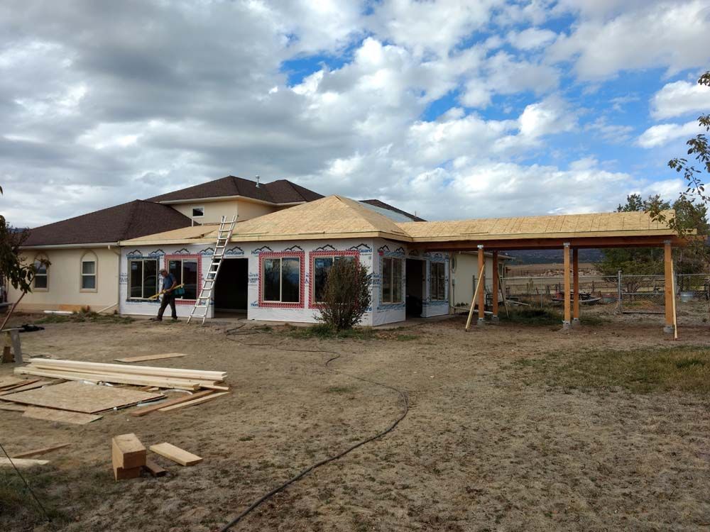 Single-story house under construction with workers, unfinished roof, and materials in the foreground