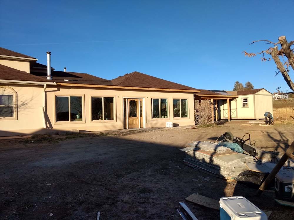 Single-story house with patio doors, bare yard, and construction debris under a clear blue sky