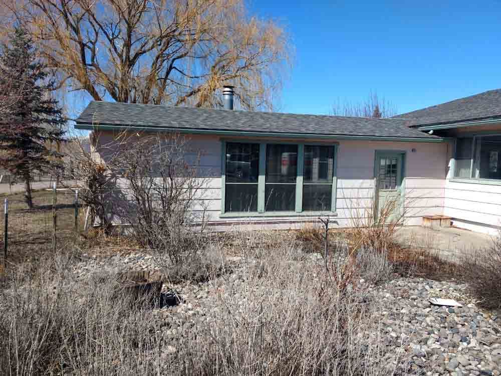 Single-story house exterior with large window and dry yard under a clear blue sky