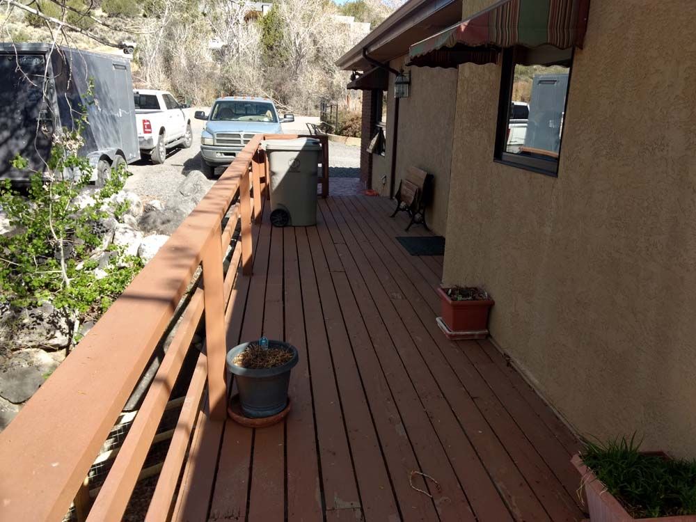 Wooden deck walkway beside a house, with potted plants and parked vehicles along the side.