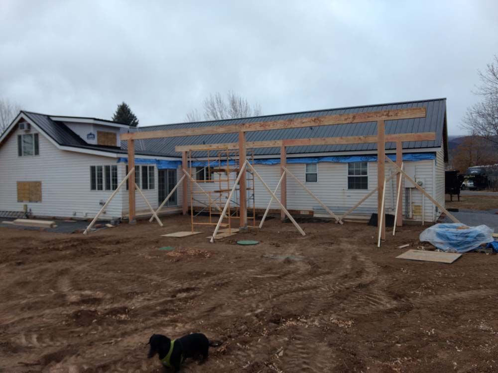 House under construction with roof framing, siding partly installed, and dirt lot in front