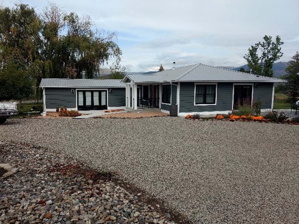 Single-story gray house with a large gravel driveway and flower beds under a cloudy sky