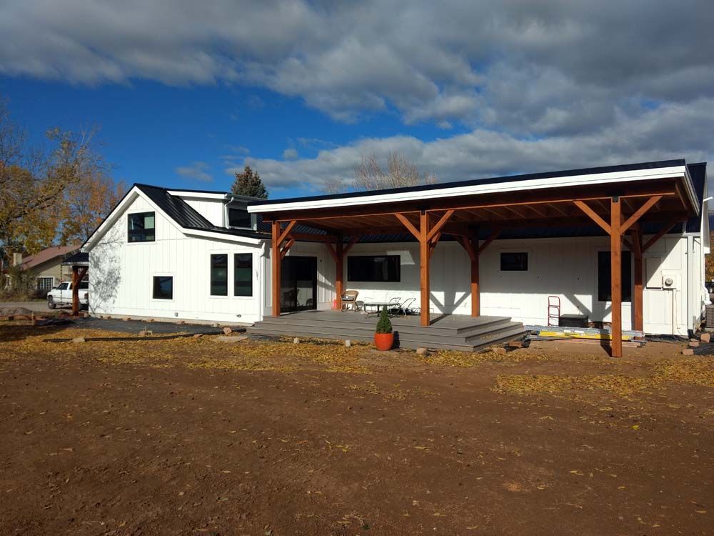 White house with a covered porch and wooden posts on a bare dirt lot under a partly cloudy sky