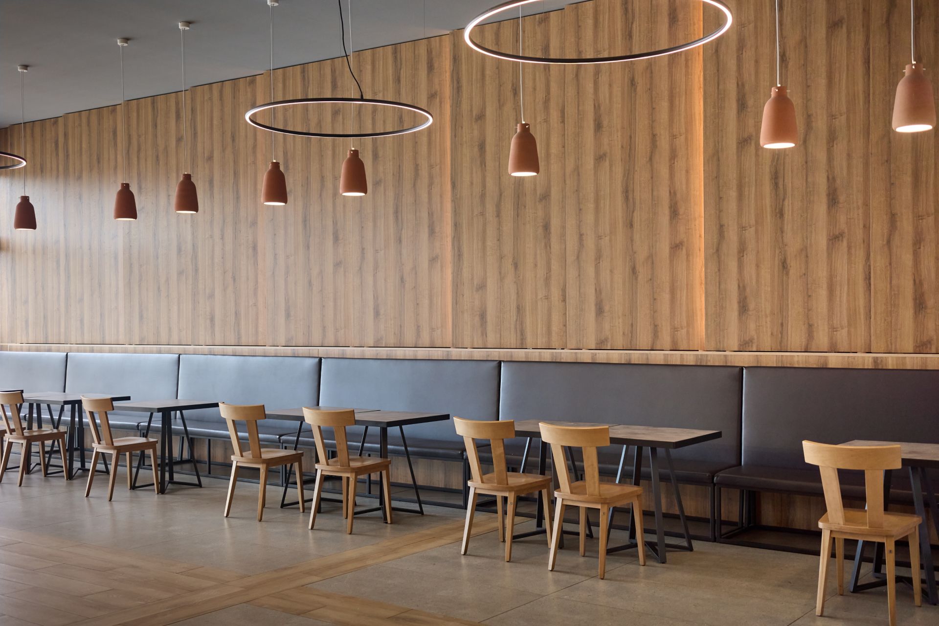 Modern café interior with wooden wall, hanging pendant lights, and empty tables and chairs