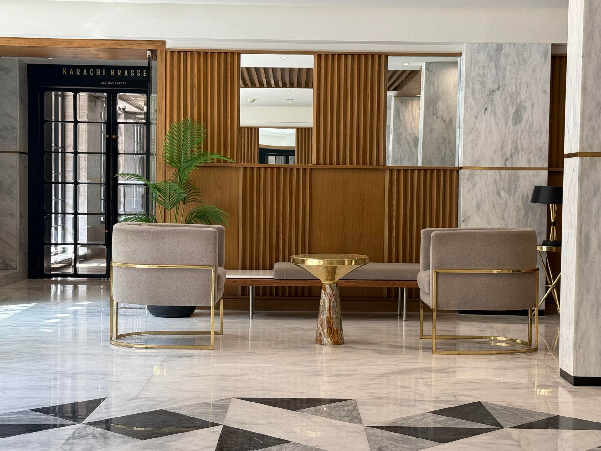 Modern lobby seating area with two beige chairs, a gold table, wood slat wall, and marble floor tiles