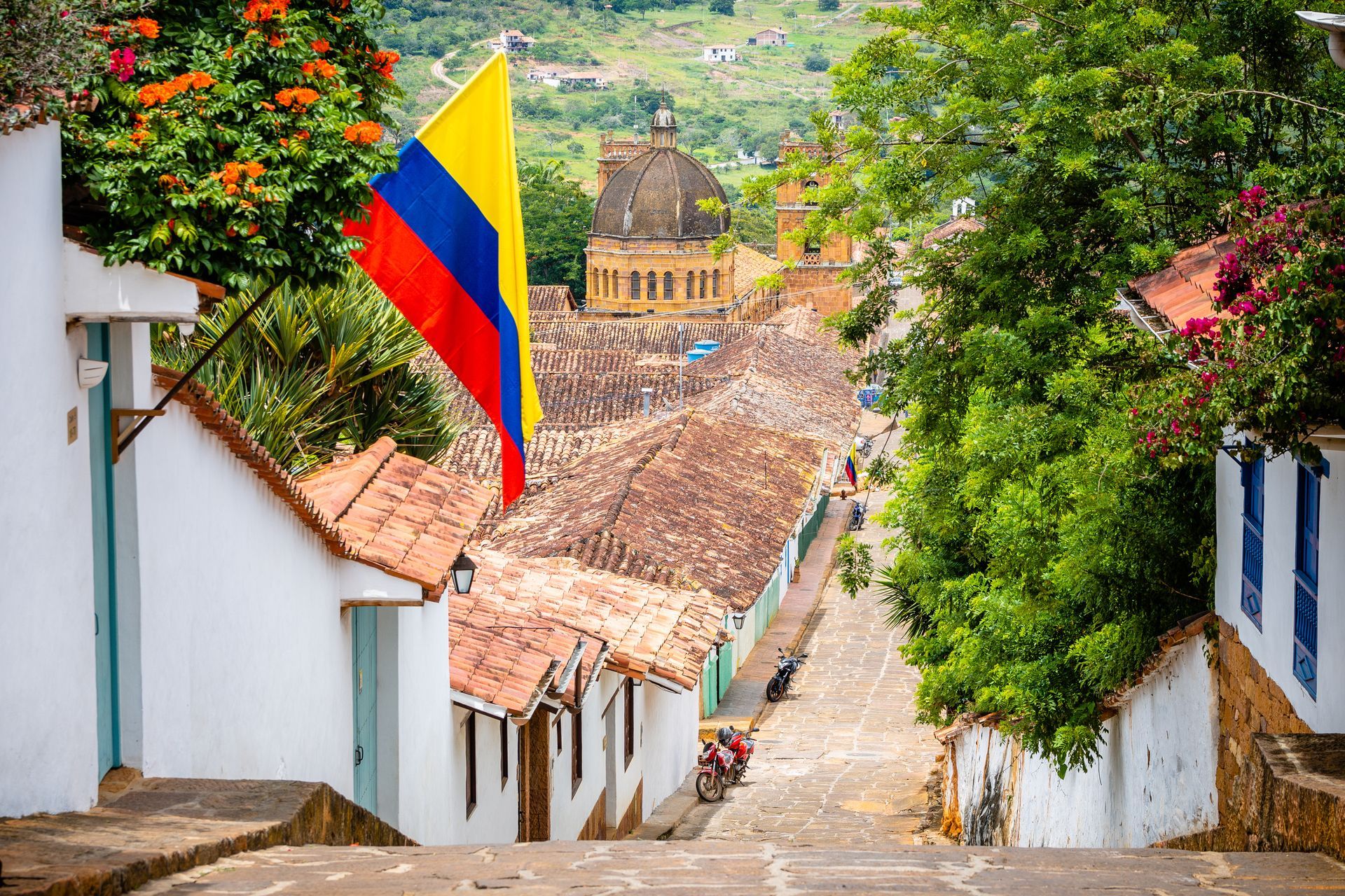 Calle colonial con bandera de Colombia y cúpula histórica al fondo, destino turístico imperdible para viajar por Colombia.