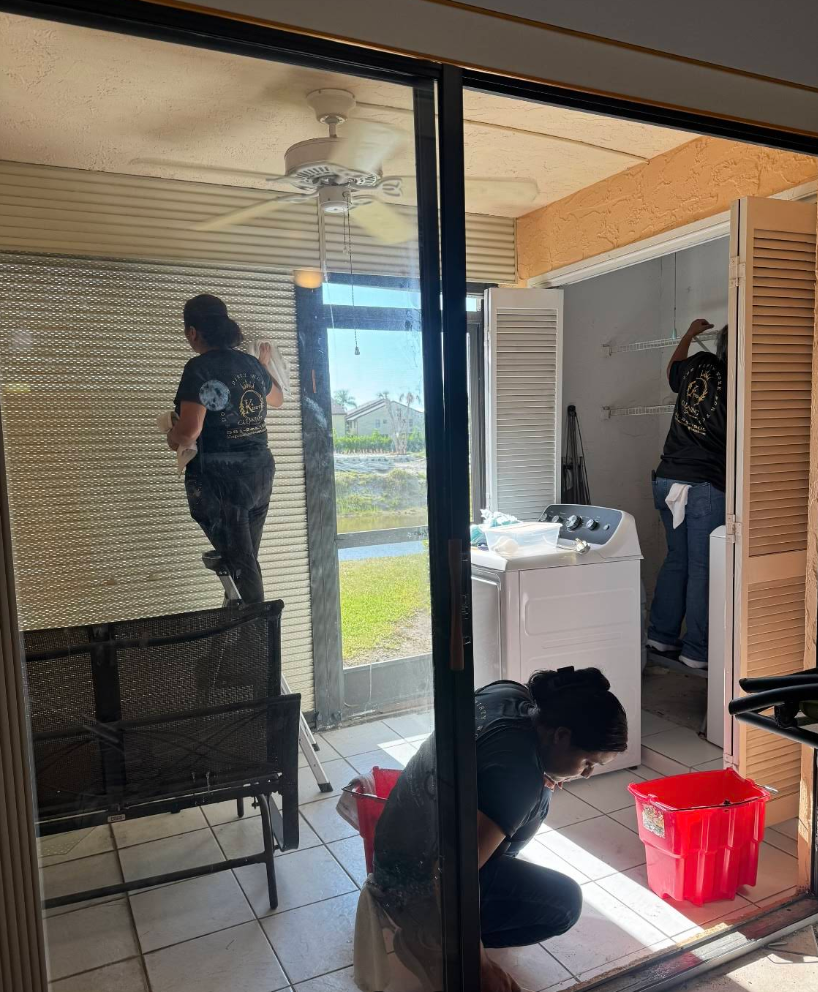 People cleaning a screened-in porch with a washer and dryer visible. One person is on a bench cleaning the screen.