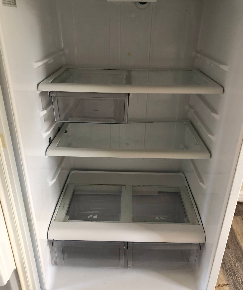 Empty white refrigerator interior with glass shelves and drawers.